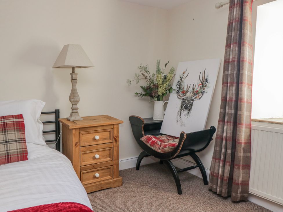 A bedroom with a bed, nightstand, lamp, chair, and painting at High Ickenthwaite Farmhouse Ulverston