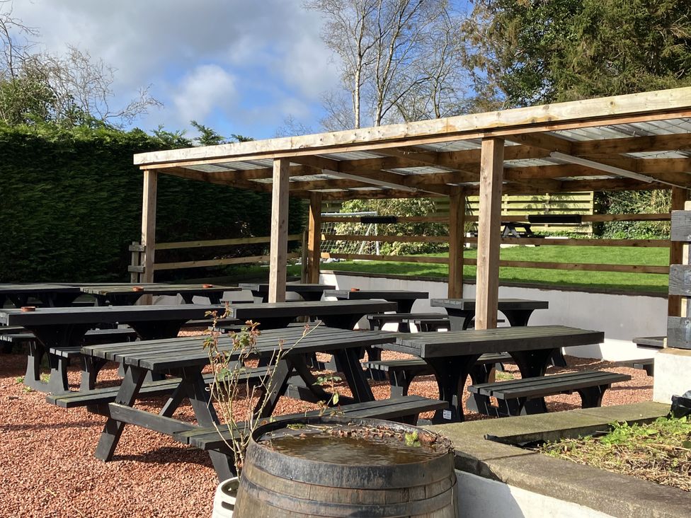 A covered outdoor seating area with tables and benches at The Steading in Castle Douglas