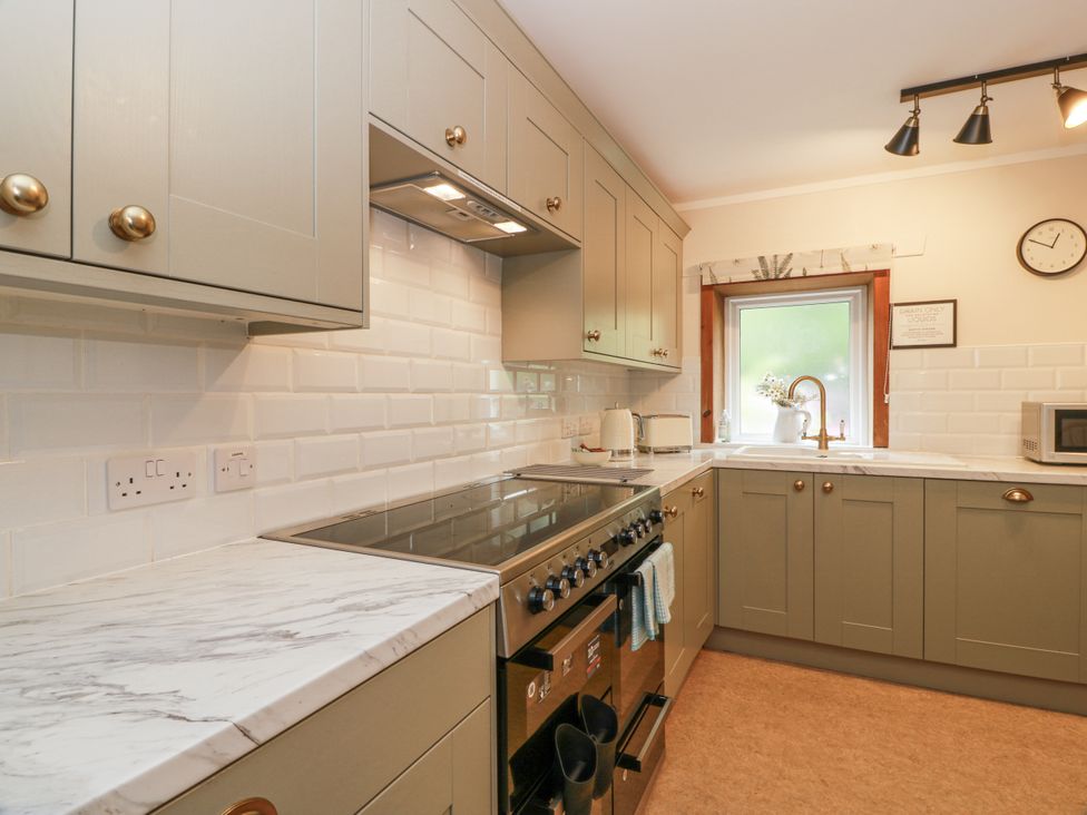 A kitchen with cabinets, stove, microwave and sink at The Steading in Castle Douglas