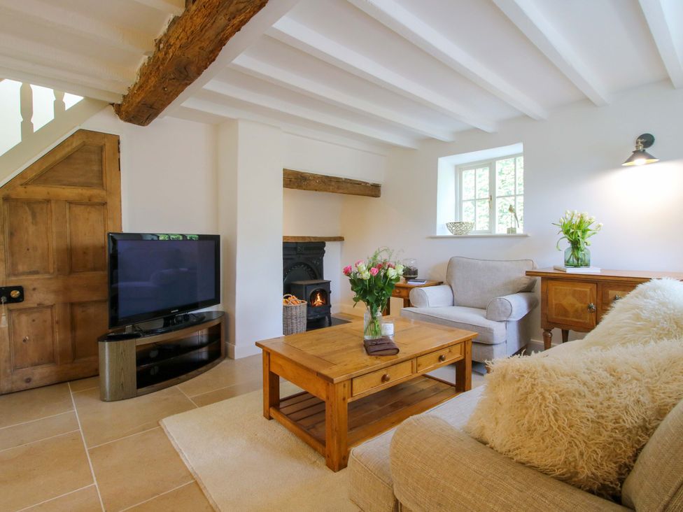 A living room with a television, a sofa, and flowers on a table at 5 Shrewsbury Road in Much Wenlock
