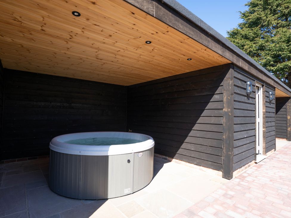 A covered outdoor area with a hot tub next to a black wooden building at Coral Cottage in Kessingland