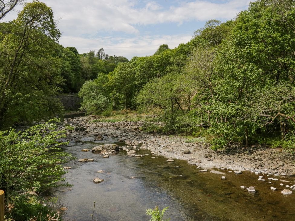 A shallow river with rocks and trees along the banks at Elter Luxury Pod in Keswick