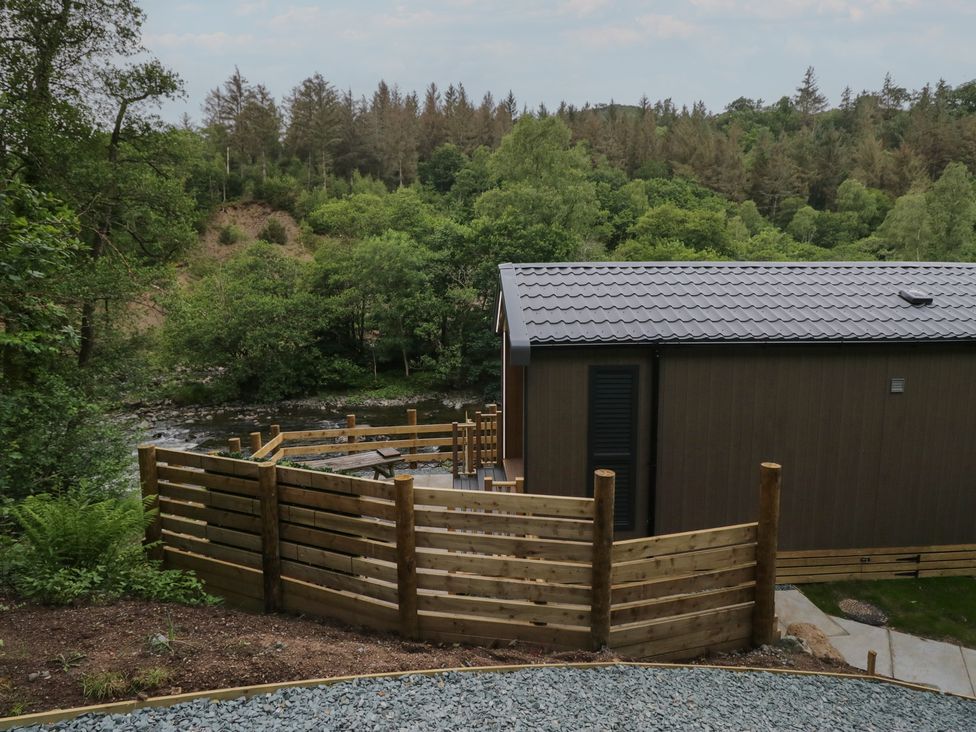 An outdoor area with a wooden building and fence by a river at Dubs Luxury Family Pod in Keswick