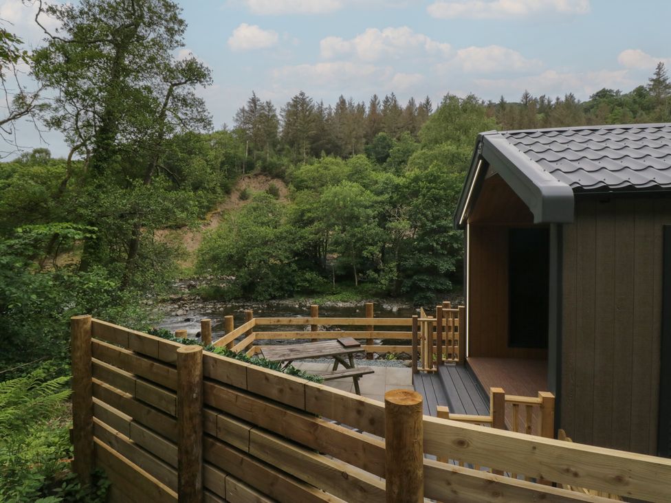 An outdoor area with a deck and table near a river at Dubs Luxury Family Pod in Keswick