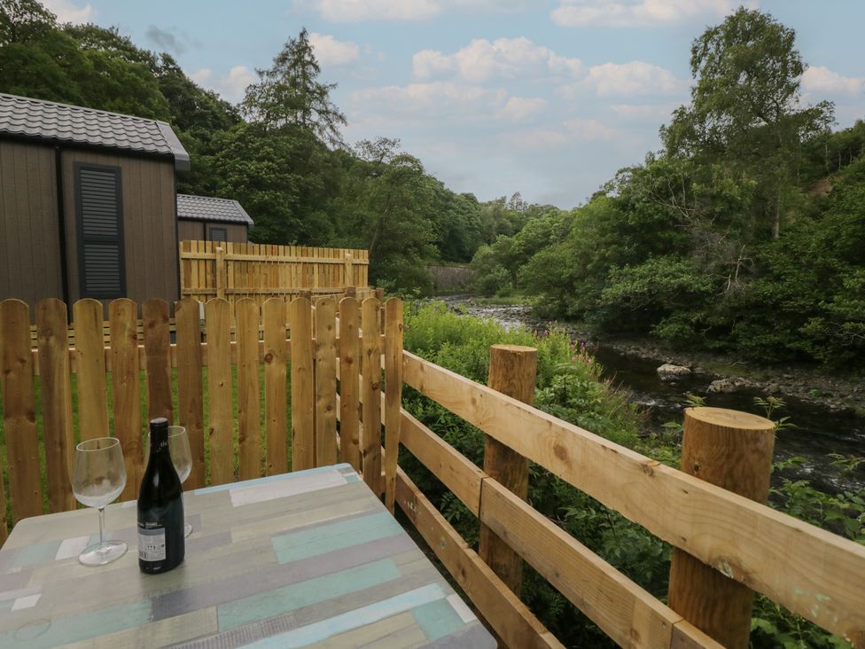 An outdoor seating area with a table, glasses, and a bottle at Woof Luxury Family Pod in Keswick