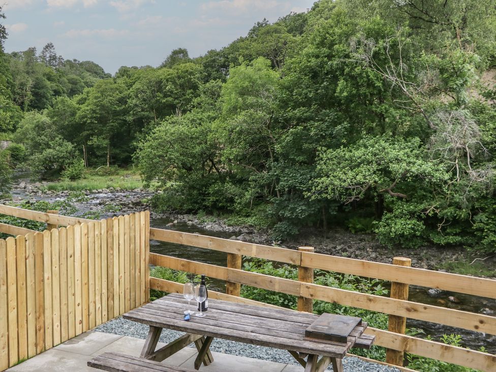 An outdoor seating area with a table and chairs near a river at Sail Luxury Family Pod in Keswick