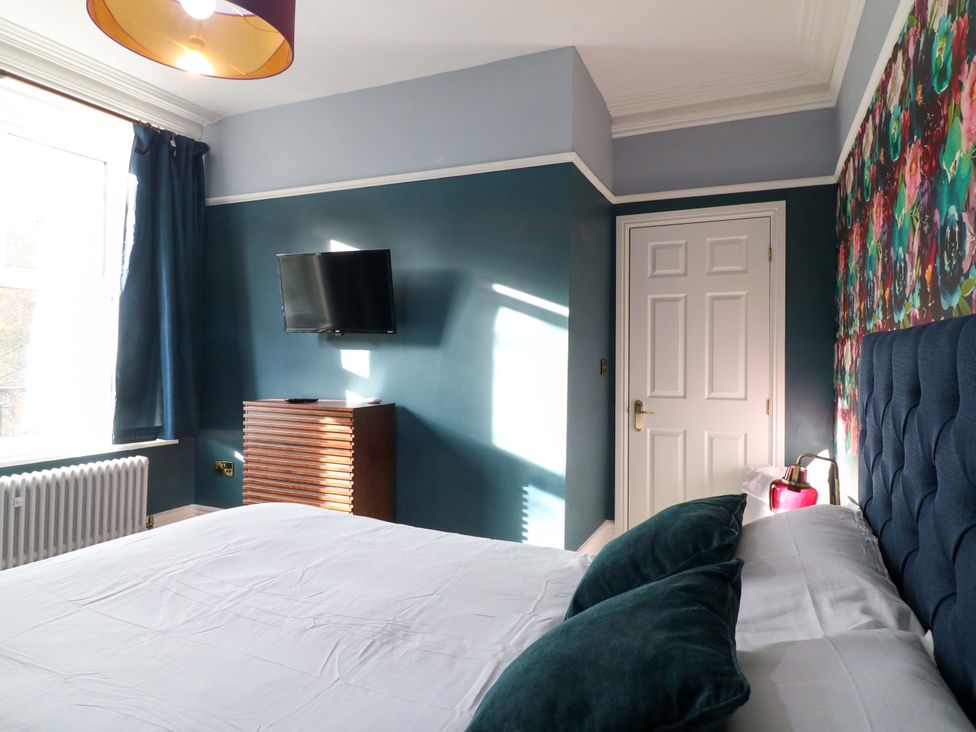 A bedroom with a bed, dresser, television, and curtains at High Peaks Villa in Buxton
