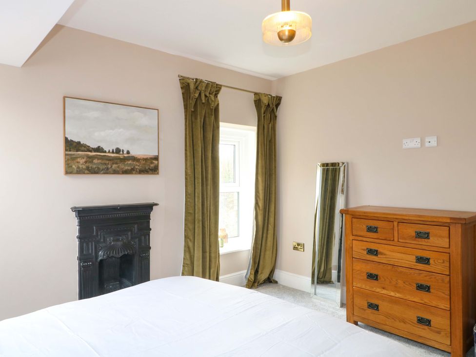A bedroom with a bed, dresser, curtains, and a mirror at High Peaks Villa in Buxton