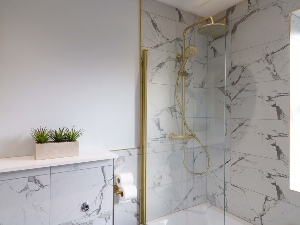 A shower with glass door and gold fixtures at High Peaks Villa in Buxton