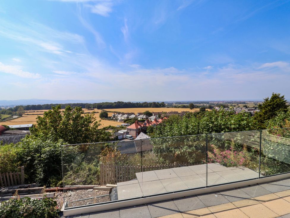 A patio area with glass railing overlooking fields and houses at Ael Y Bryn in Dyserth