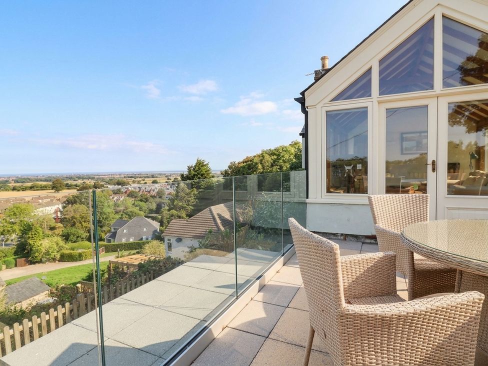 An outdoor terrace with a glass railing and seating at Ael Y Bryn Dyserth