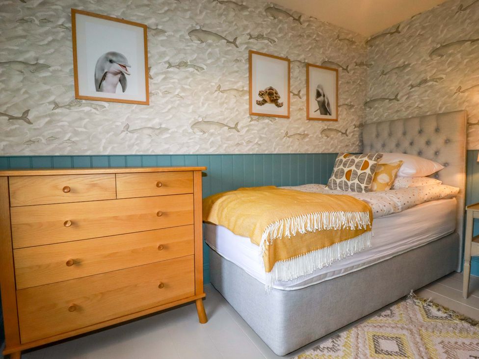 A bedroom with a bed, dresser, and pictures on the wall at Vosporth Villa, Newquay
