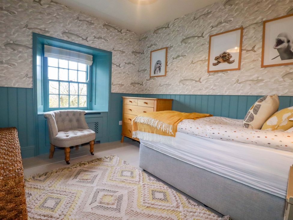 A bedroom with a bed, chair, and chest of drawers at Vosporth Villa in Newquay
