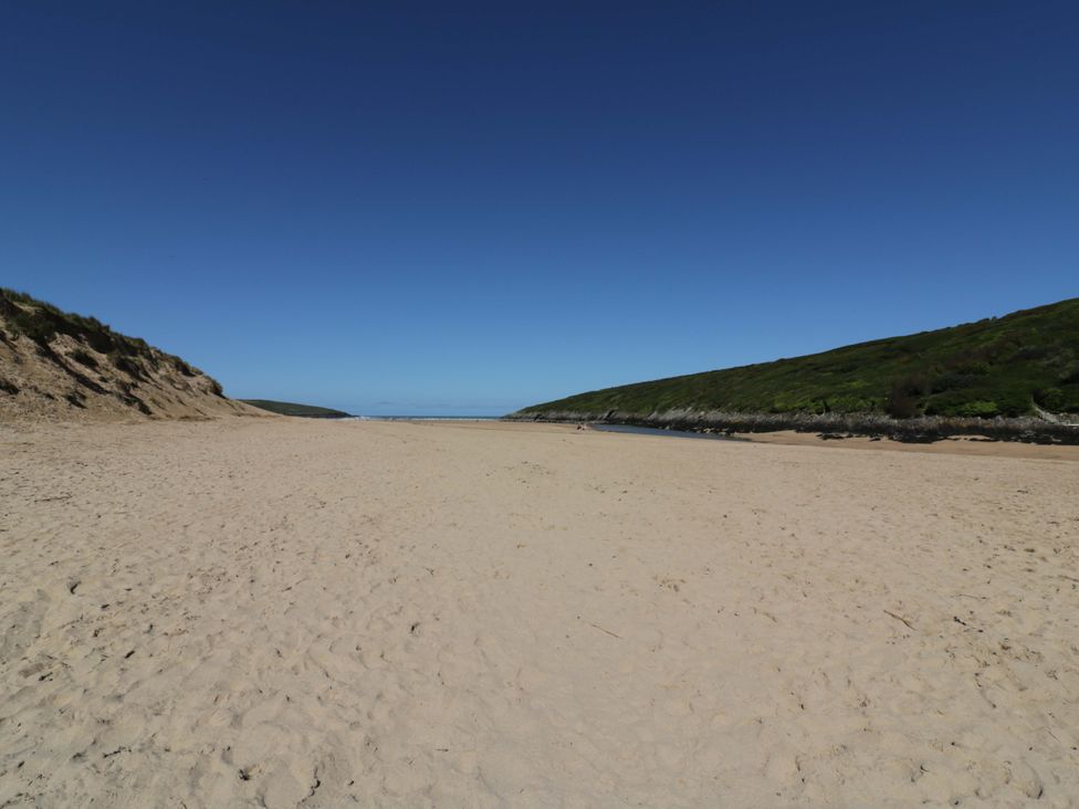 A beach with sand and hills on either side at Vosporth Villa in Newquay