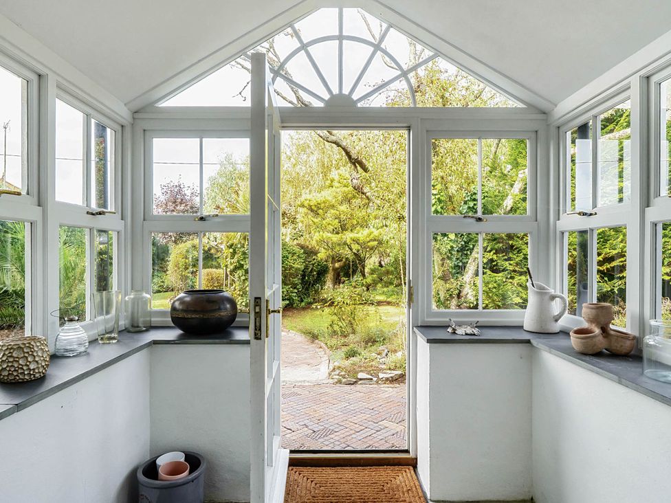 A conservatory with a door opening to a garden at Vosporth Villa in Crantock