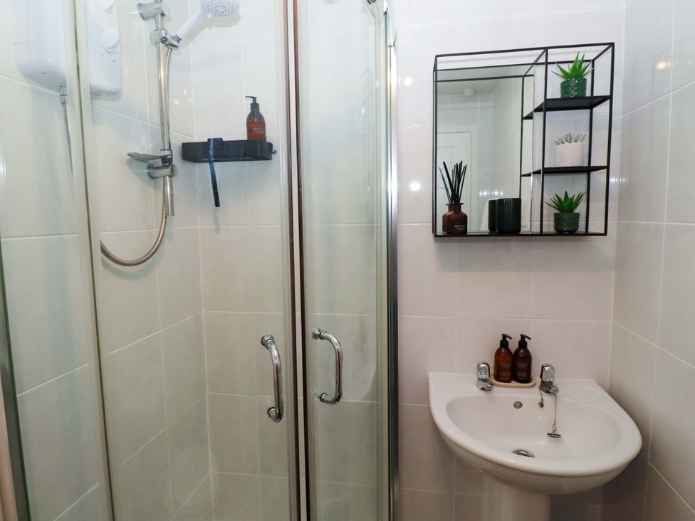 A bathroom with a shower, sink, mirror and shelf at North Sands in Beadnell
