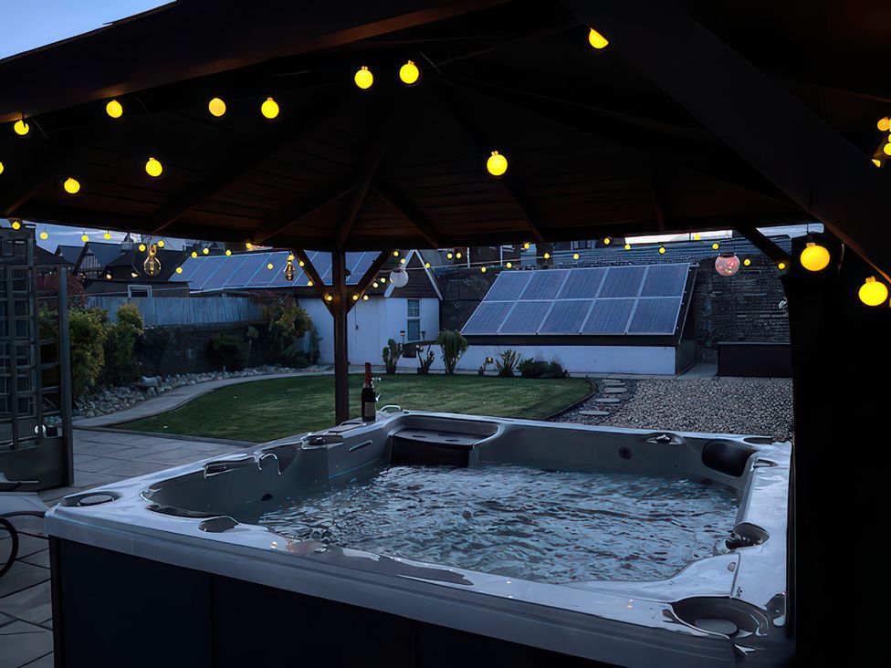 A hot tub in a garden with solar panels and string lights at Marine House Pevensey Bay