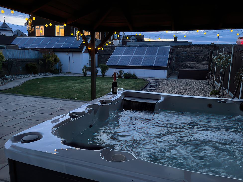 A hot tub with a bottle of wine in the garden at Marine House Pevensey Bay