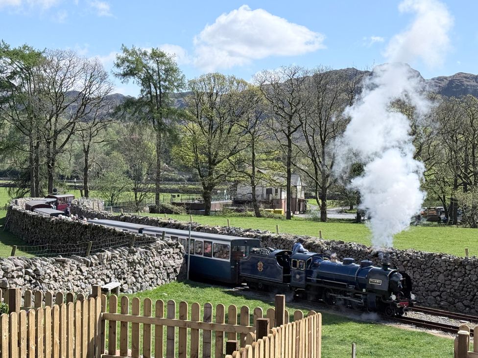 A steam train on the railway with a stone wall and trees in the background at Dakota near Boot