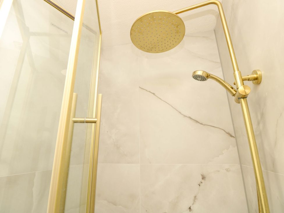A shower with a glass door and gold fixtures at Glebe Garth in Chale near Niton