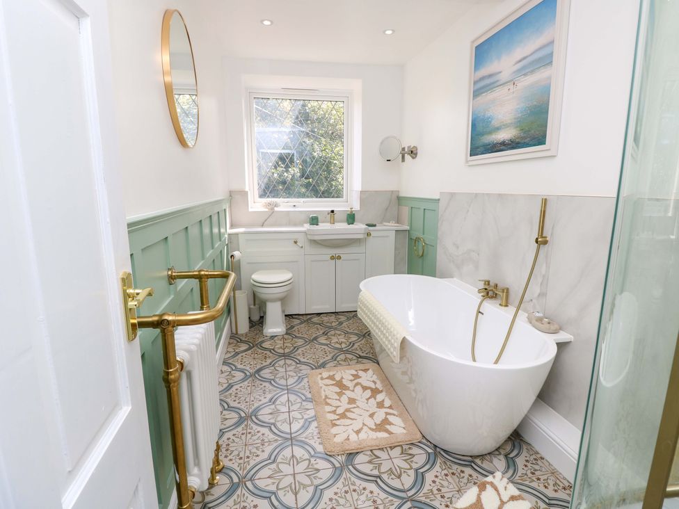 A bathroom with a tub, toilet, sink, and mirror at Glebe Garth in Chale near Niton