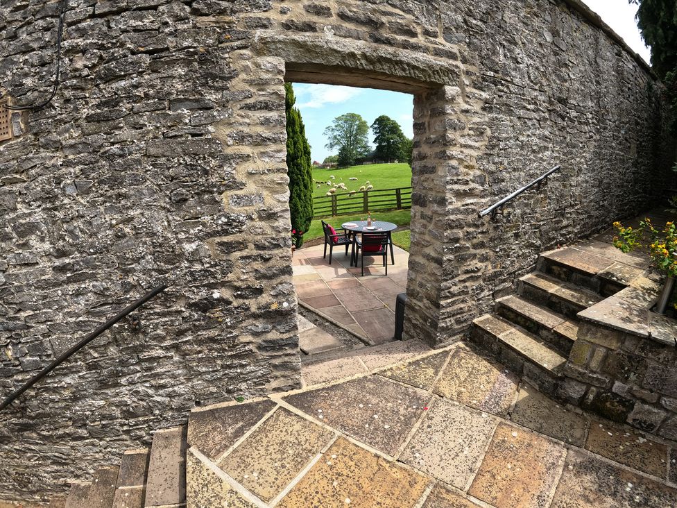 An outdoor area with a table and chairs visible through a stone doorway at Poppy's Footprint Leyburn