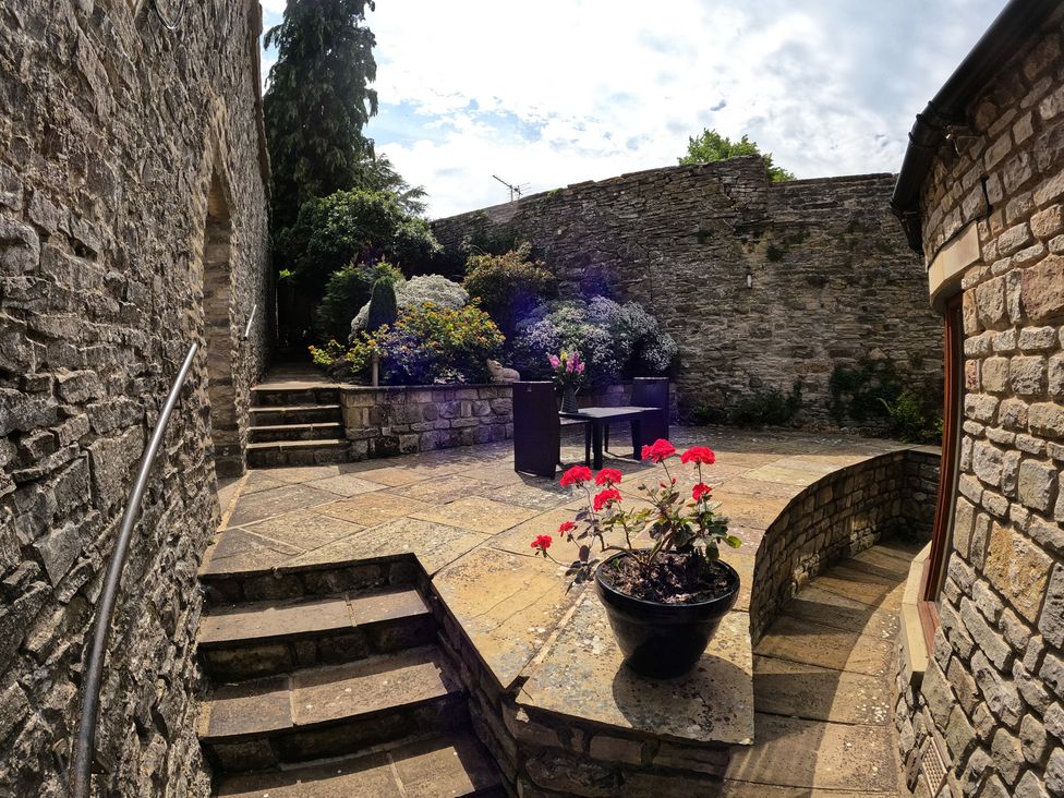 An outdoor area with a table and chairs near stone walls at Poppy's Footprint in Leyburn