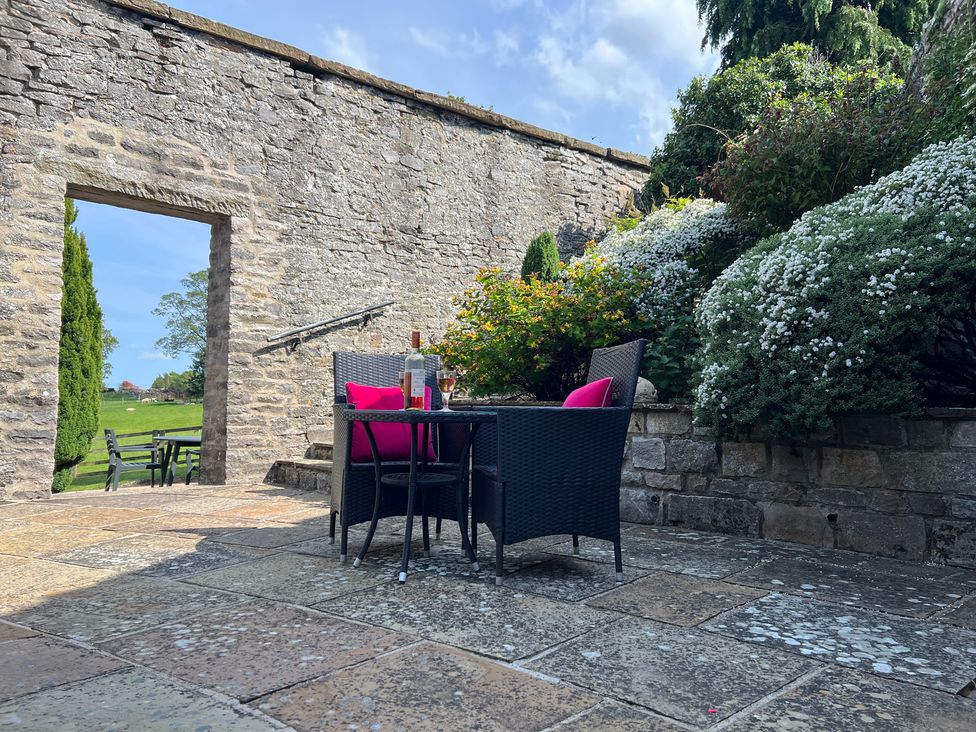 A garden with a table and chairs near a stone wall at Poppy's Footprint in Leyburn