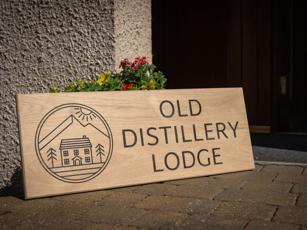 A sign for Old Distillery Lodge with flowers at the entrance