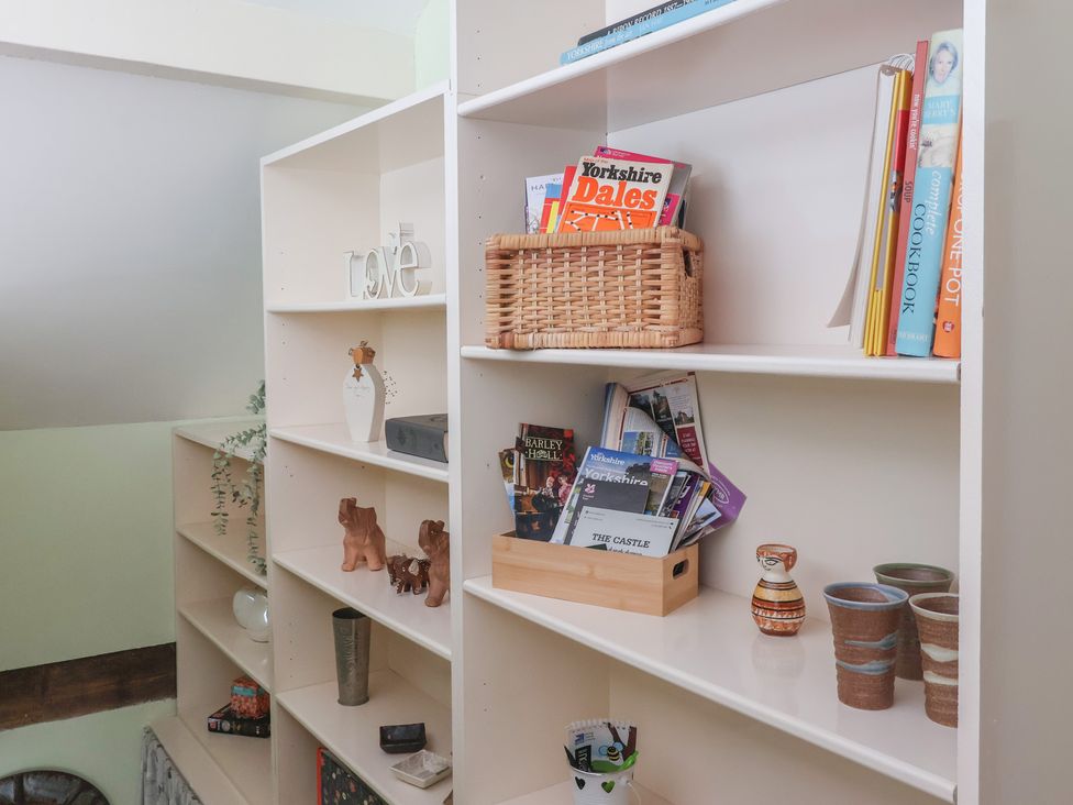 A bookshelf with books, magazines, and decorative items at Figgy Cottage in Ripon