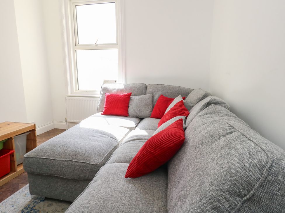 A corner of a living room with a gray sectional sofa and red cushions near a window at Seaside House in Weymouth