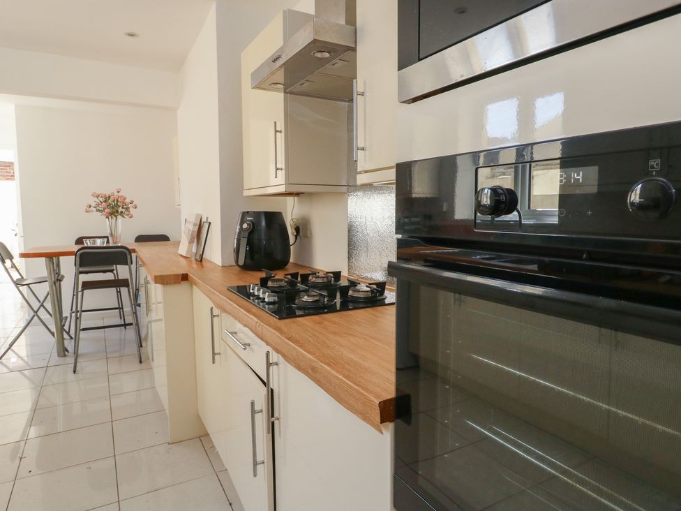 A kitchen with a built in oven and stove a black air fryer a wooden countertop and a dining table with chairs and flowers at Seaside House in Weymouth