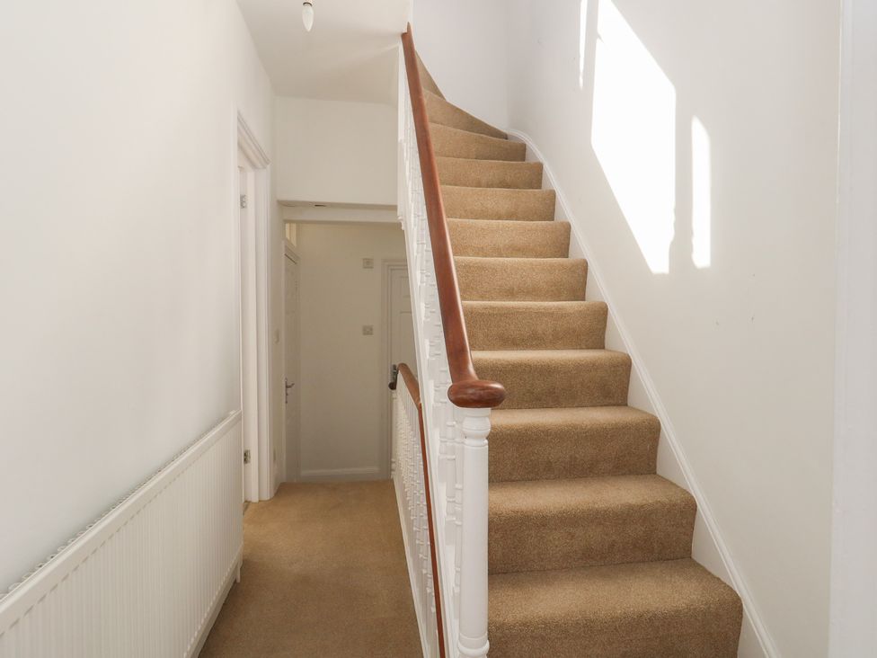 A carpeted staircase with white banisters and wooden handrail in a hallway with white walls and doors at Seaside House in Weymouth