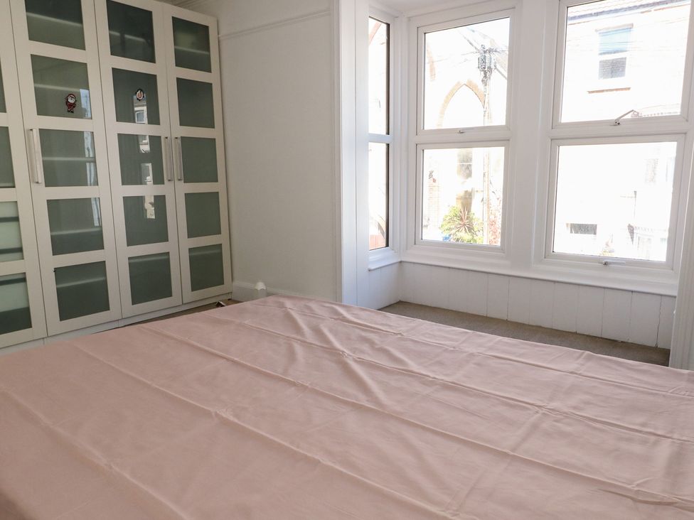 A bedroom with a bed covered by a pink sheet near a large window and a white wardrobe with frosted glass doors at Seaside House in Weymouth