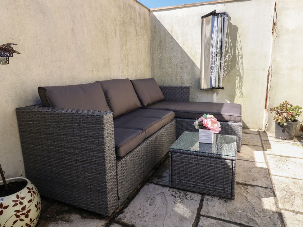 An outdoor patio area with a rattan sofa and coffee table with flowers and potted plants against a corner wall