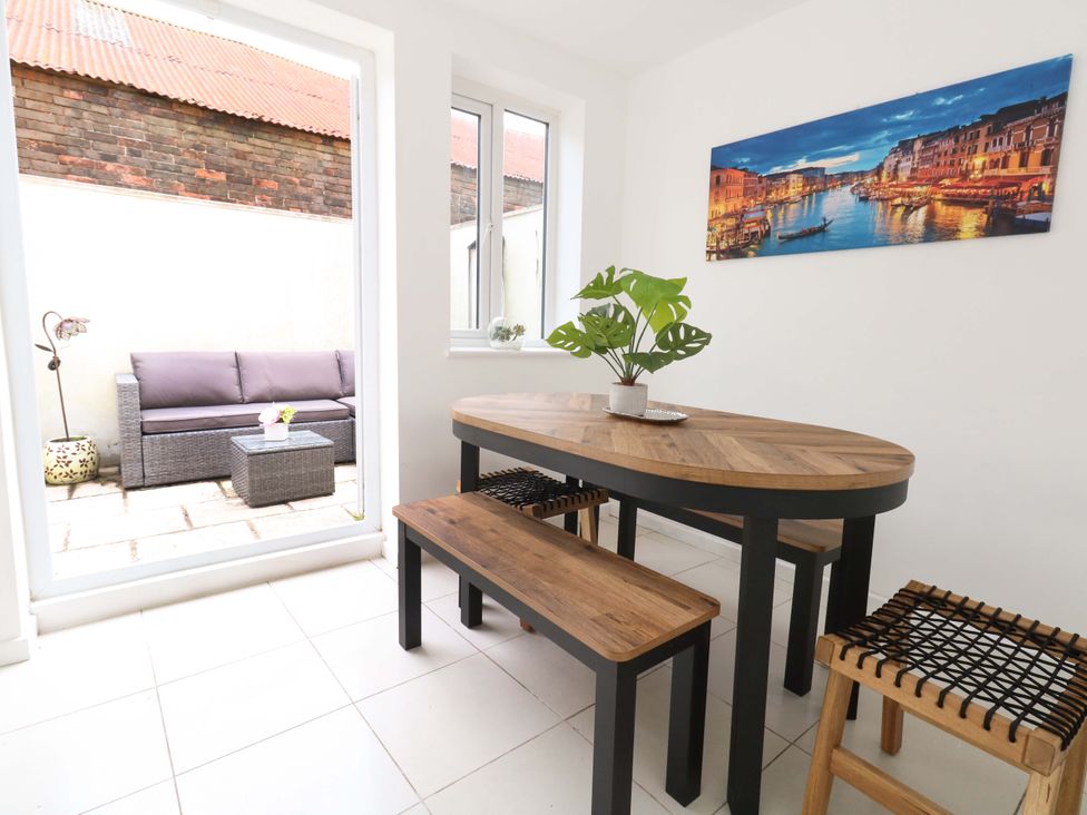 A dining room with a table, benches, and a view of the outdoor patio at Weymouth Seaside House in Weymouth