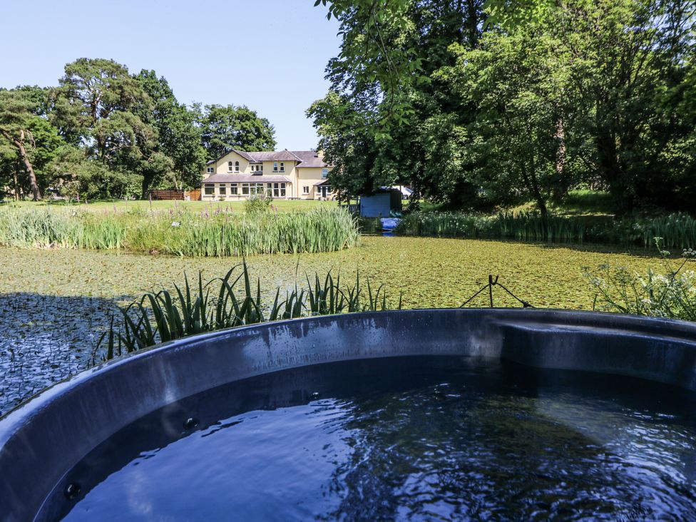 A view of a hot tub and pond with a house in the background at Glanrannell Park House in Llanwrda