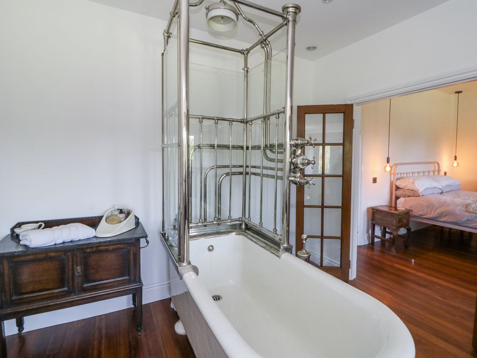 A bathroom featuring a bathtub and a shower with a wooden cabinet at Glanrannell Park House in Llanwrda