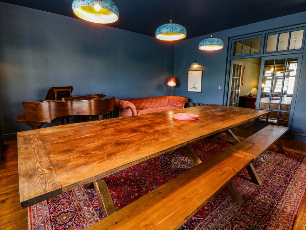 A dining room with a wooden table and piano at The Retreat at Glanrannell Park House in Llansawel