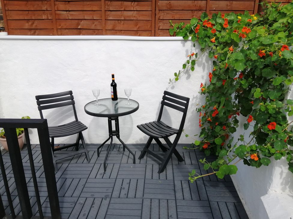 A patio with a table and chairs, wine bottle and glasses at Colliers Cottage in Cinderford