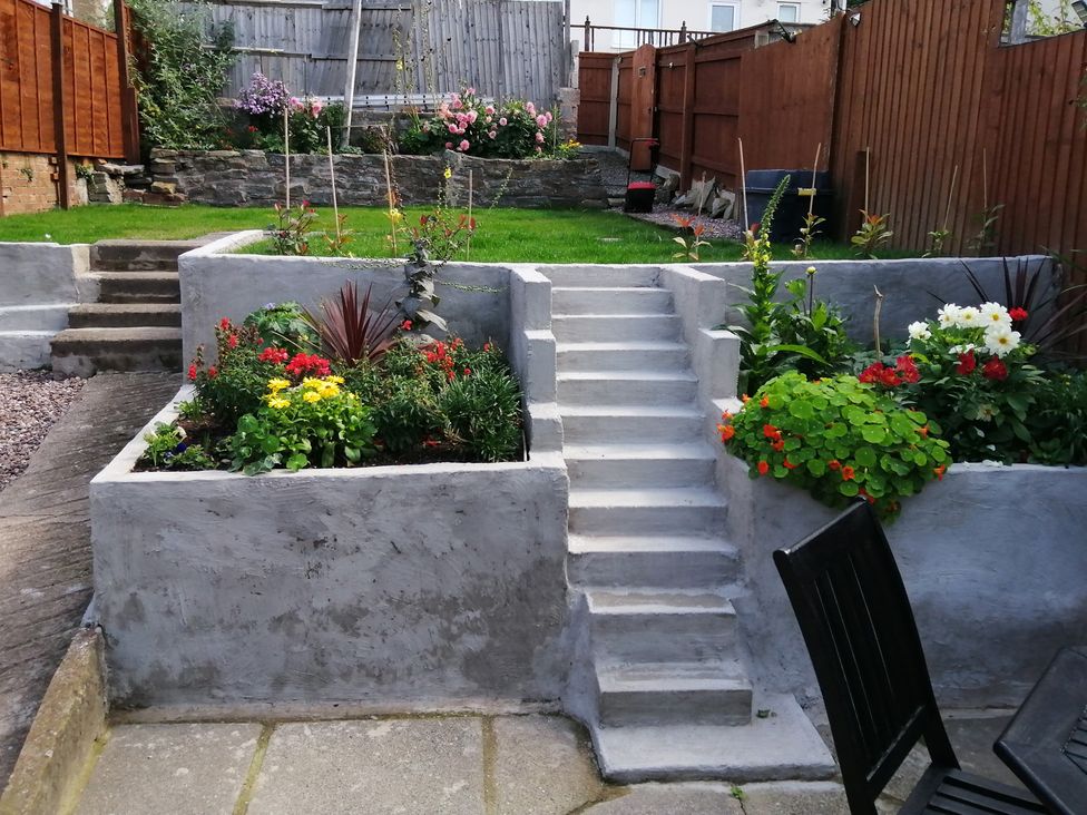 A garden with flower beds, grass, and stairs at Colliers Cottage in Cinderford