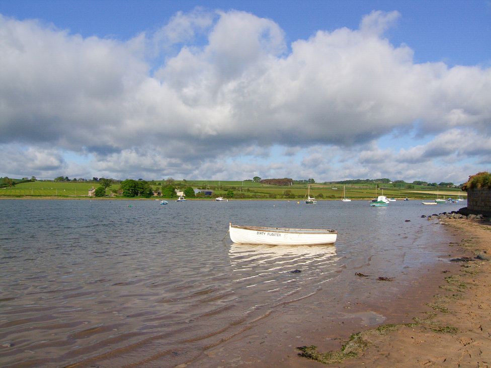 A boat on water near a shore with grass and clouds at Seafield Coach House Alnmouth