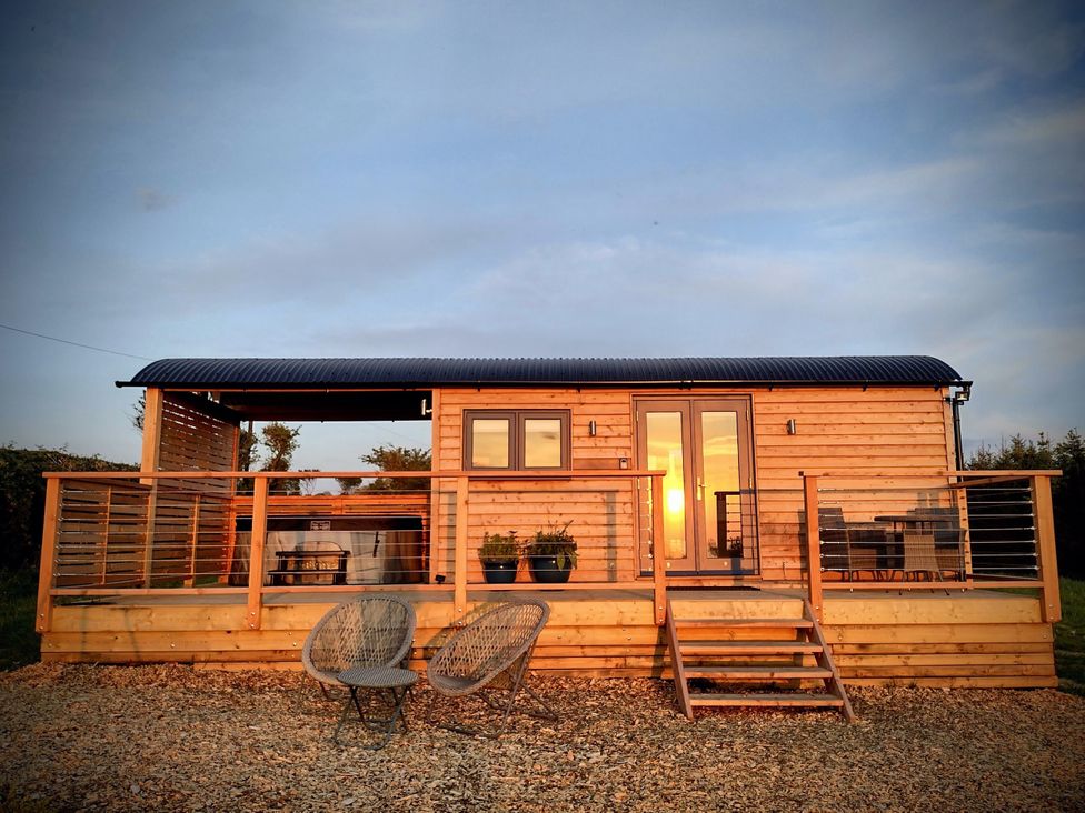 A wooden cabin with a deck and chairs at Fir Tree Shepherd's Hut Llanon