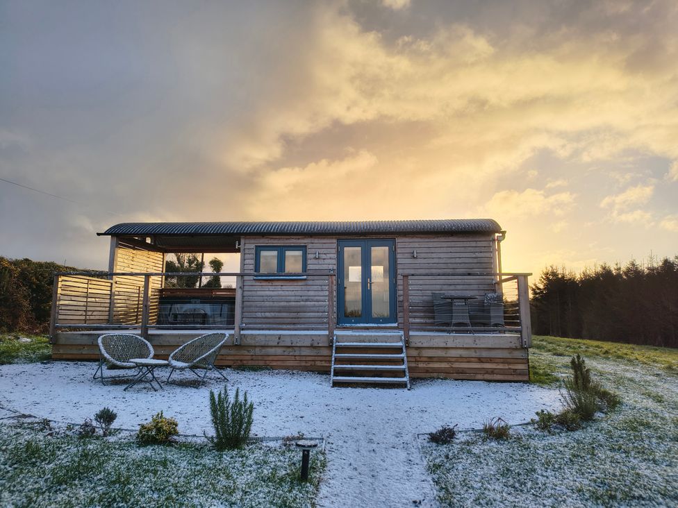 A wooden hut with chairs on a deck at Fir Tree Shepherd's Hut in Llanon