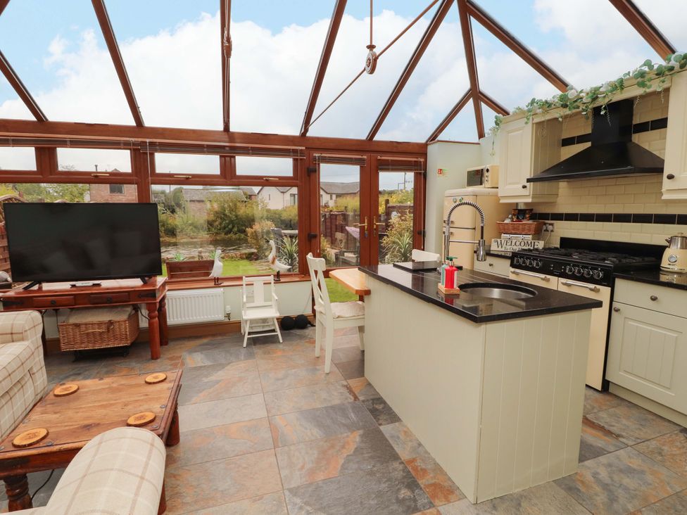 A conservatory with a kitchen island and seating area at Beckside Cottage in Penrith