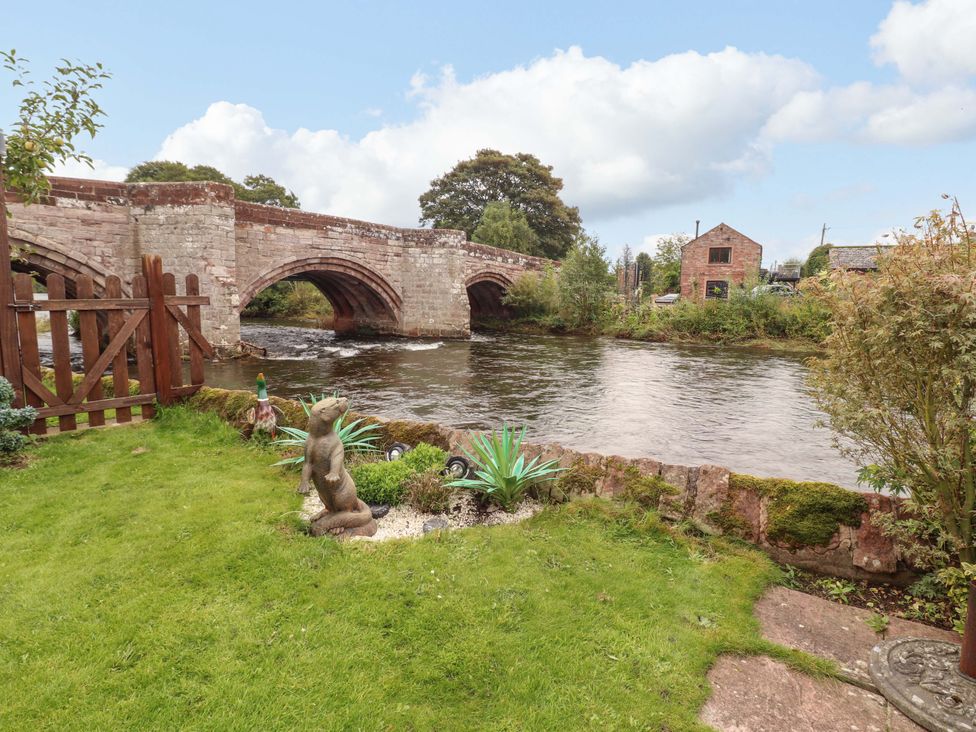 A garden with a river and a bridge at Beckside Cottage in Penrith