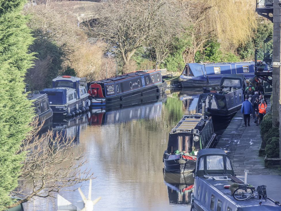 A canal with narrow boats and people walking along in Waters Edge Skipton