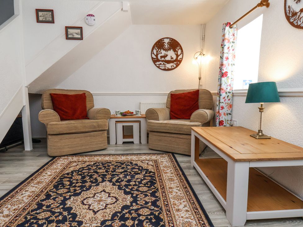 A sitting area with two armchairs with red cushions a patterned rug and a wooden coffee table with lamp at Wayside Farm Dairy Cottage Cloughton near Burniston