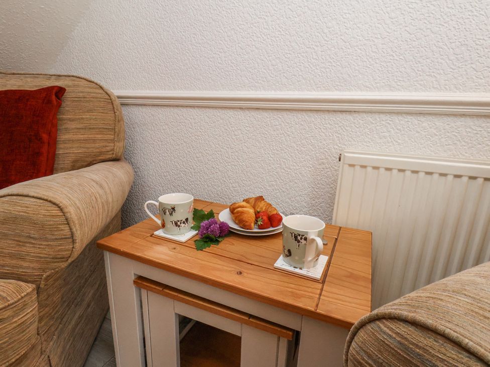 A wooden side table with two animal print mugs, a plate with croissants and strawberries, flowers between two fabric armchairs at Wayside Farm Dairy Cottage Cloughton near Burniston