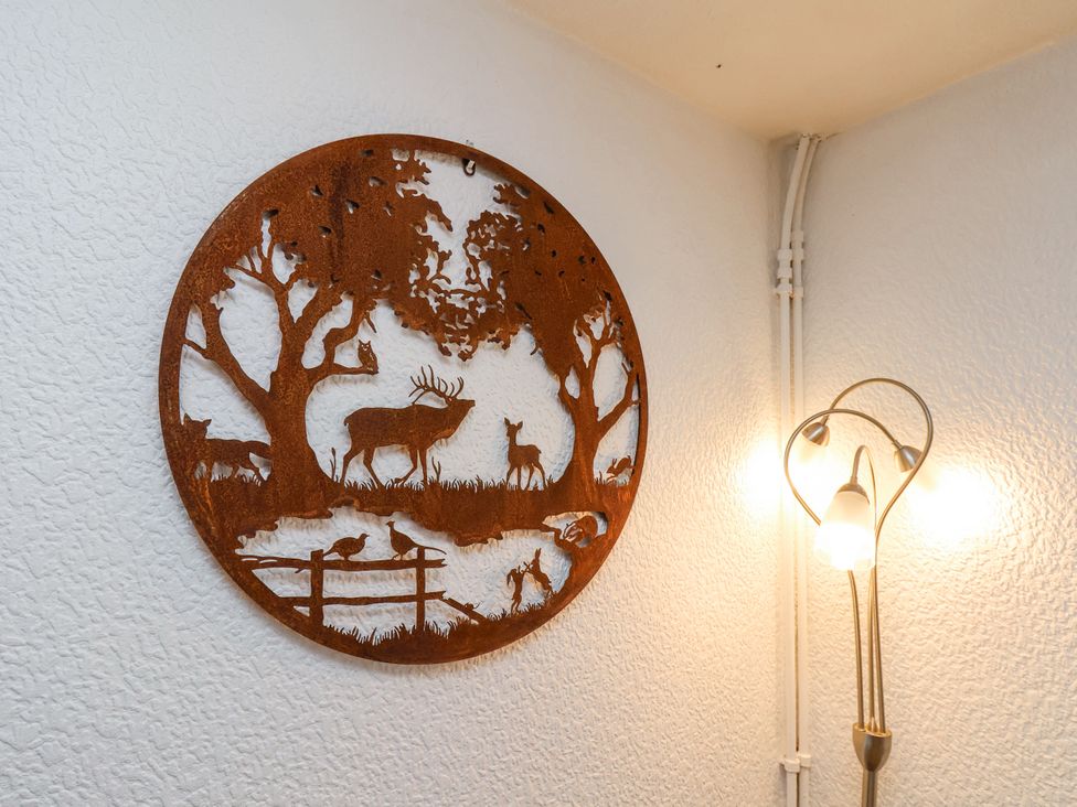 A metal wall art depicting deer and birds next to a floor lamp in a corner of a room at Wayside Farm Dairy Cottage in Cloughton near Burniston